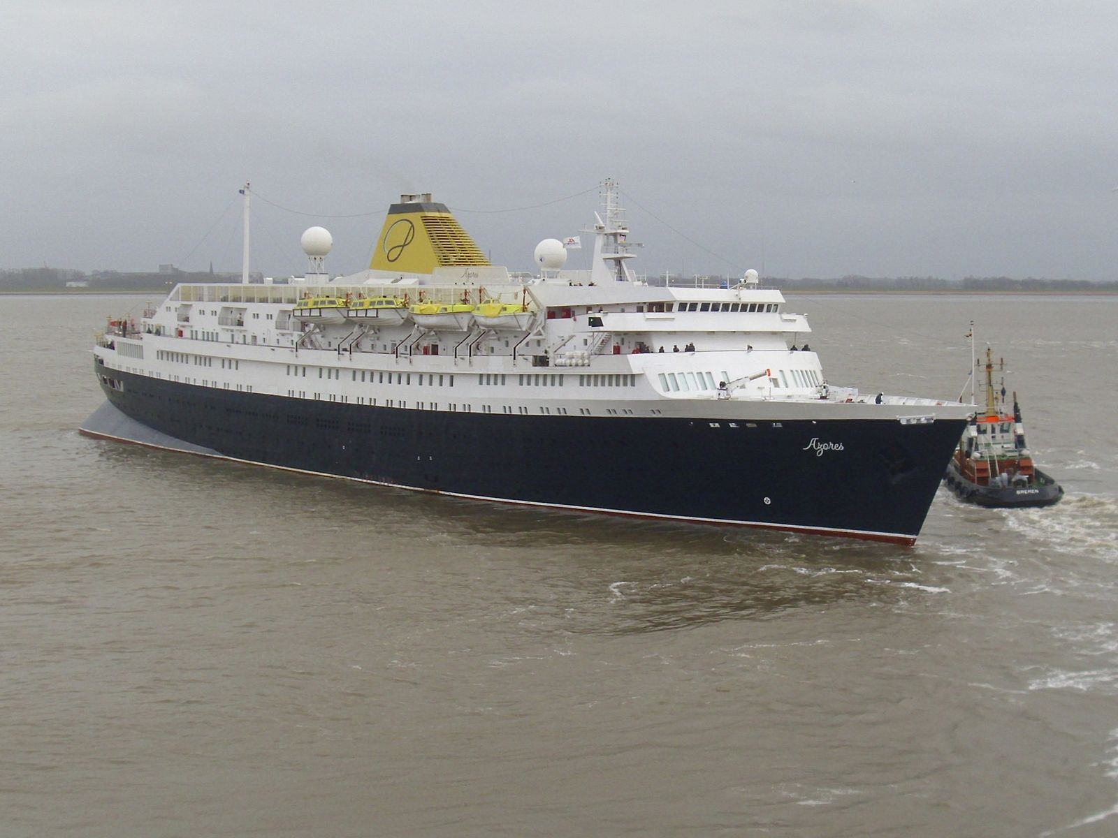 A large cruise ship departing port, showing the stacked passenger decks