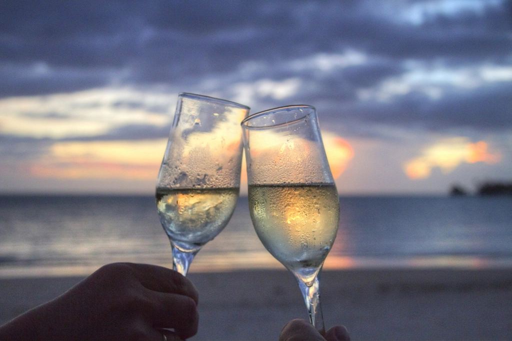 Two champagne glasses toasting at sunset on a beach, typical of couples-focused resorts