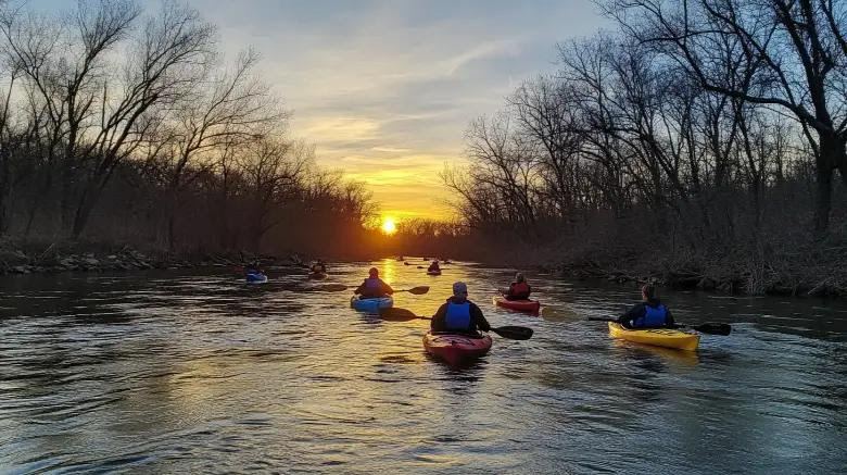Group of kayakers paddling a Kentucky river toward a golden sunset