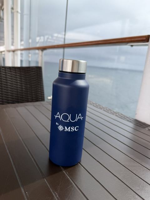An MSC-branded reusable water bottle on a deck table overlooking the sea