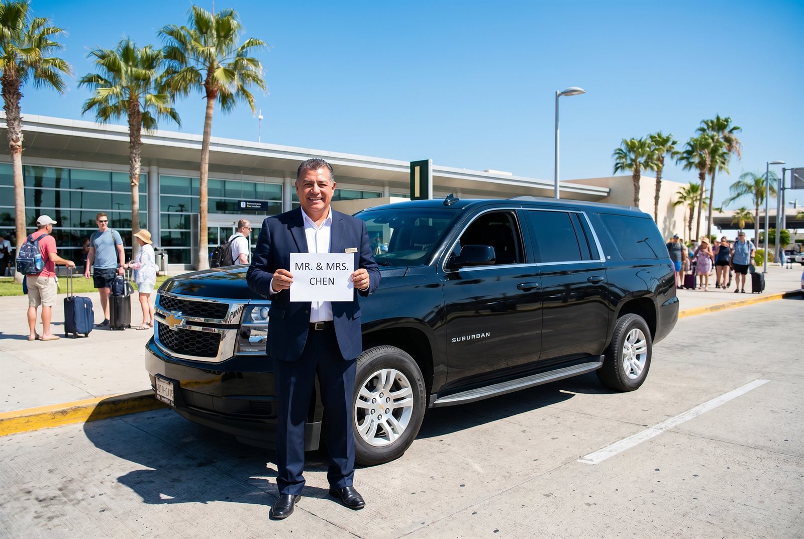 A private driver in uniform standing beside a black SUV at a sunny Mexican airport, holding a name sign for arriving guests